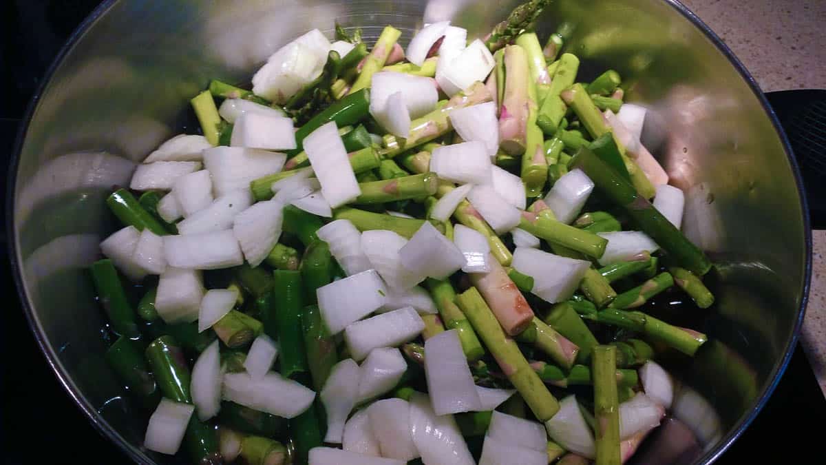 asparagus pieces and chopped onions in stock in pan