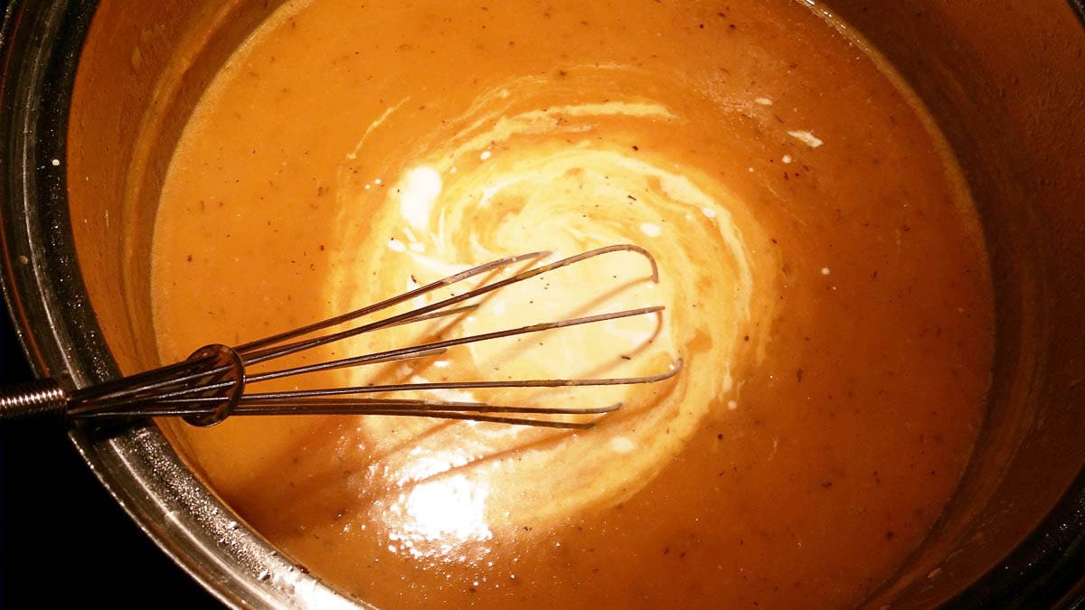 cream being whisked into pumpkin soup in pan