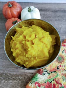 Pumpkin puree in bowl with napkin and mini pumpkins.