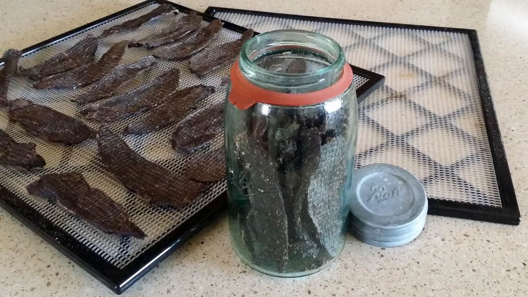 finished venison jerky on dehydrator tray and in glass jar.
