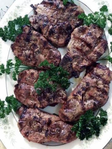 Grilled lamb chops with parsley on white platter.
