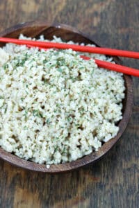 Cooked rice in wooden bowl with red chopsticks.