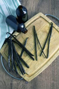 Vanilla beans and brown bottles on cutting board with blue towel.