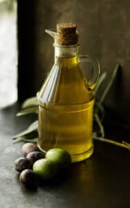 Glass jar of olive oil with olives on table.