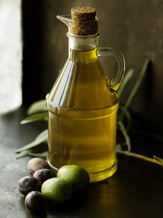 Glass jar of olive oil with olives on table.
