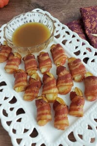 Bacon wrapped apples on white platter with bowl of caramel sauce.