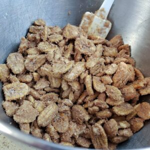Candied pecans in metal bowl with spatula.