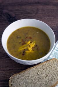 Cheeseburger Soup in white bowl with slice of bread.