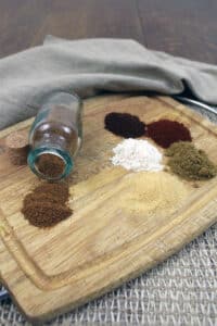 Ingredients for taco seasoning recipe on cutting board with glass jar.