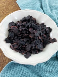 Dehydrated cherries in white bowl with blue towel.
