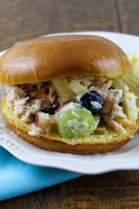 Chicken Salad with fruit and pecans on brioche bun on white plate.