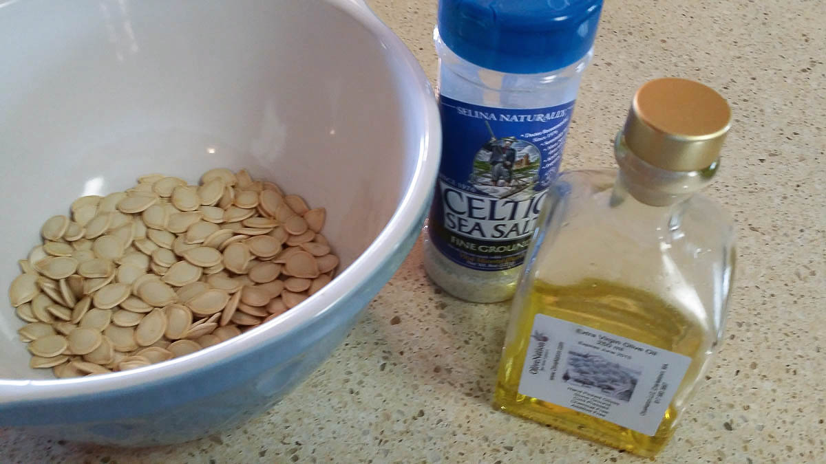 Pumpkin seeds, olive oil, and sea salt on counter.