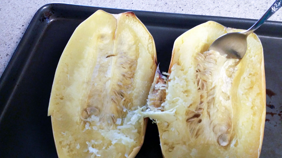Spaghetti squash halves with seeds scooped out with spoon.