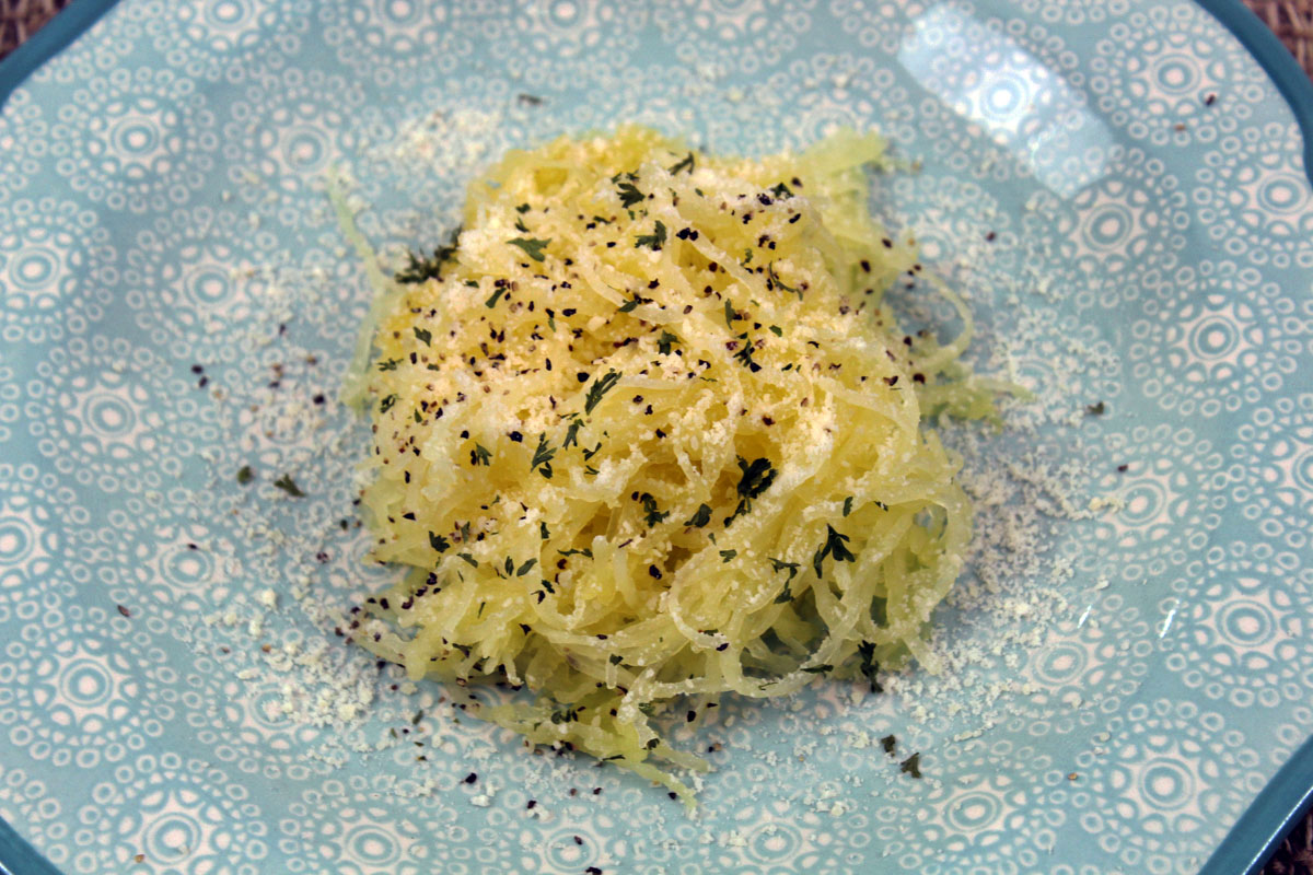 Cooked Spaghetti squash on blue plate with pepper and parmesan cheese.